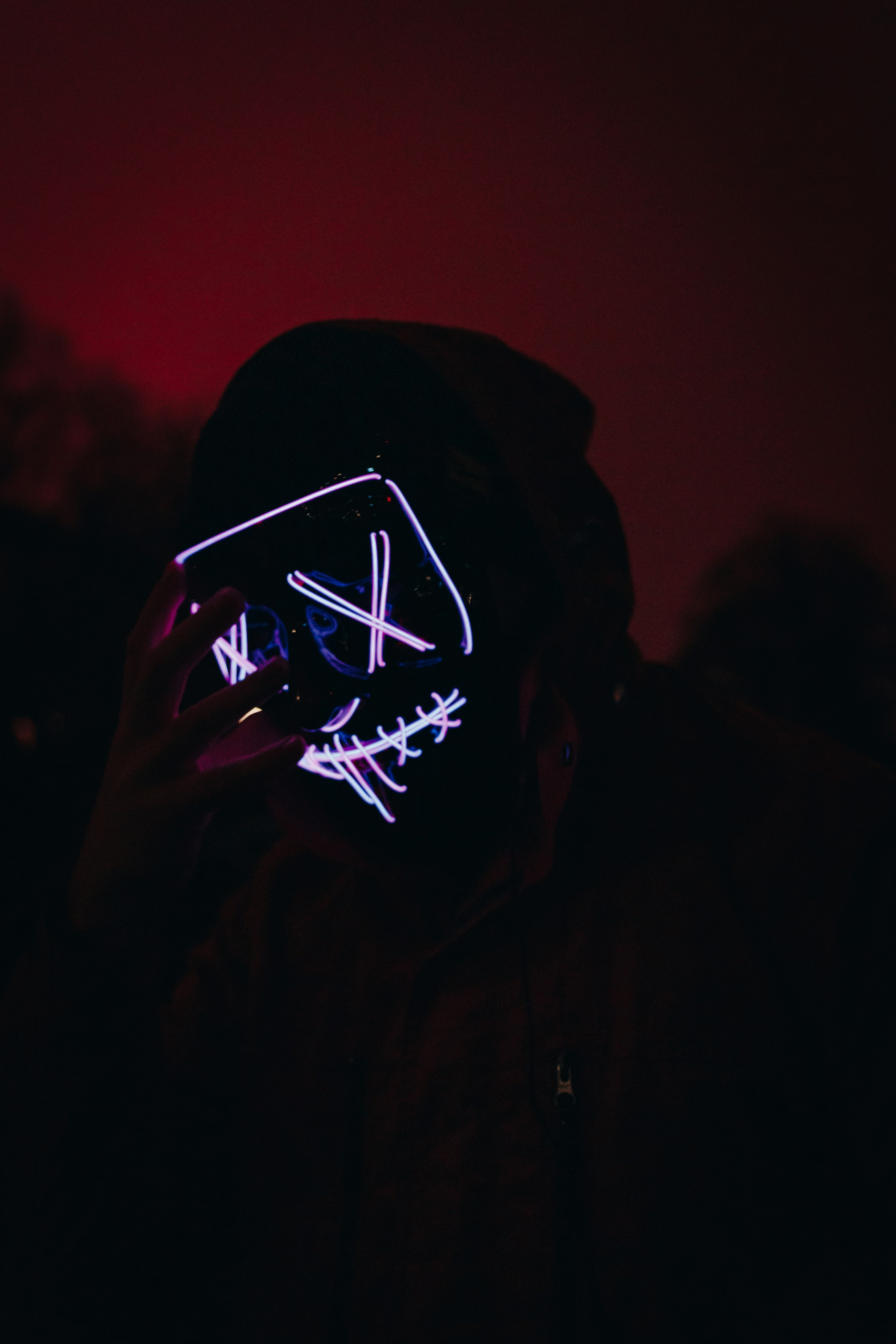 Led masked person in the dark reaching out to his face