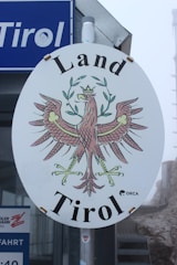 A vibrant outdoor banner displayed at a busy street corner in Tirol.