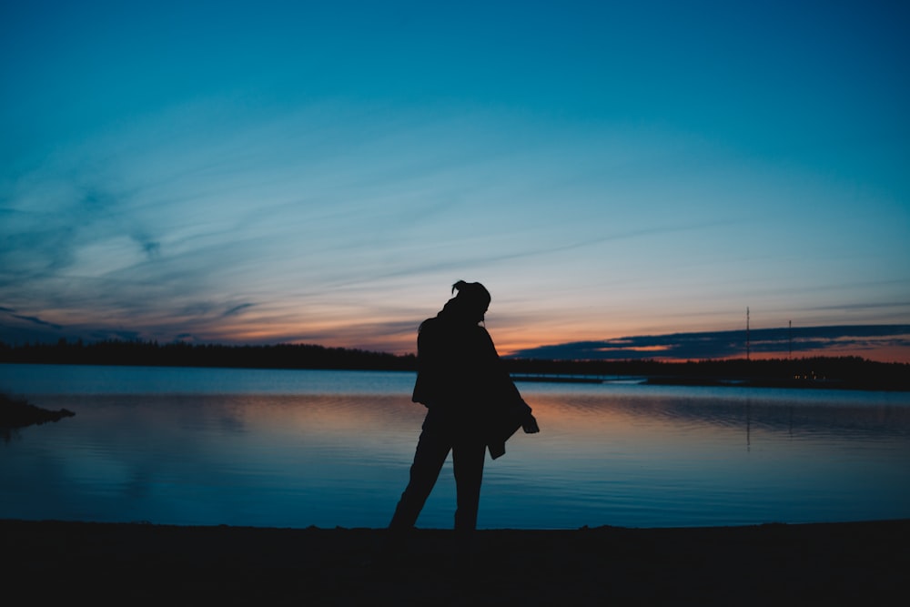 silhouette photography of unknown standing near body of water
