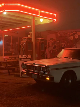 Classic vintage car parked under the glowing drive-in marquee at dusk.