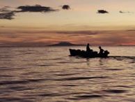 Sunset silhouette of a speedboat on calm Maldivian waters with islands in the distance.