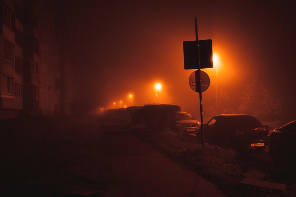 a foggy street at night with cars parked on the side of the road