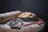 A bowl filled with glazed cookies is set on a wooden board dusted with powdered sugar. Nearby, a wooden rolling pin, metal cookie cutters, and a candy cane are visible, all suggesting a baking theme.