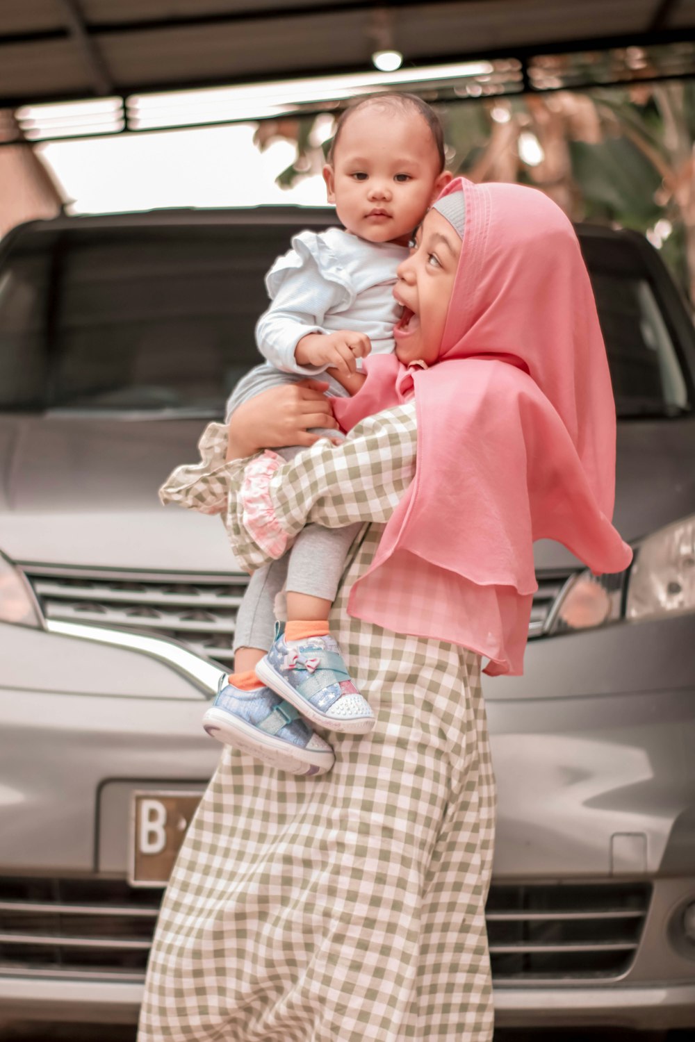 a woman holding a baby in front of a car