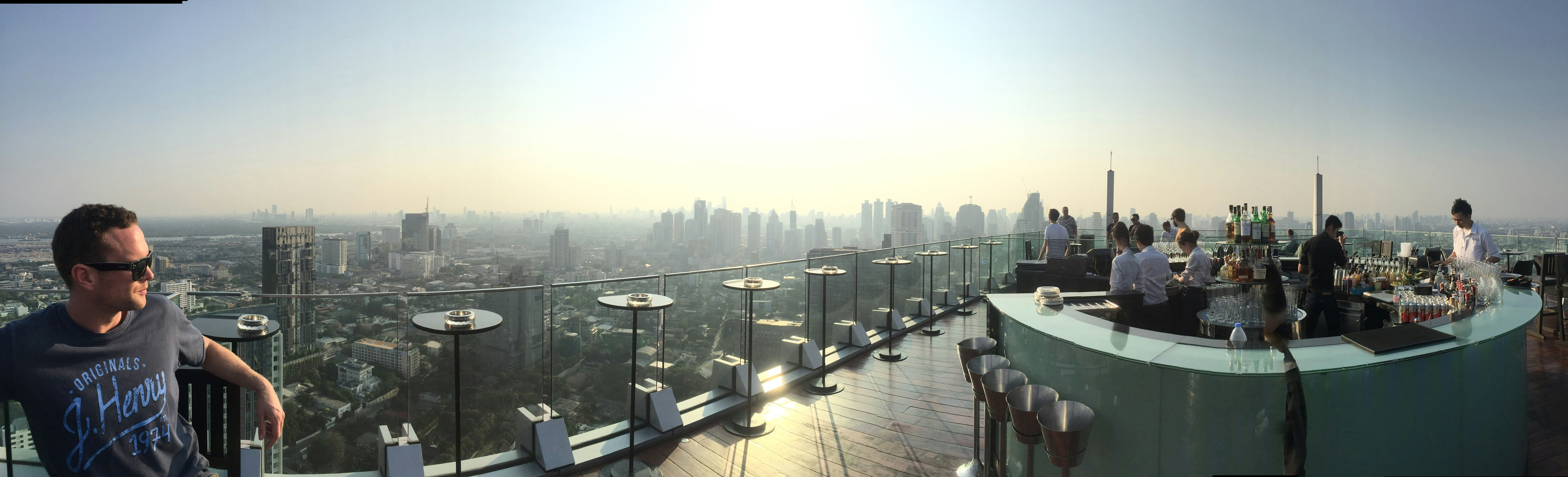 Man at rooftop bar, relaxed confident posture, city skyline background