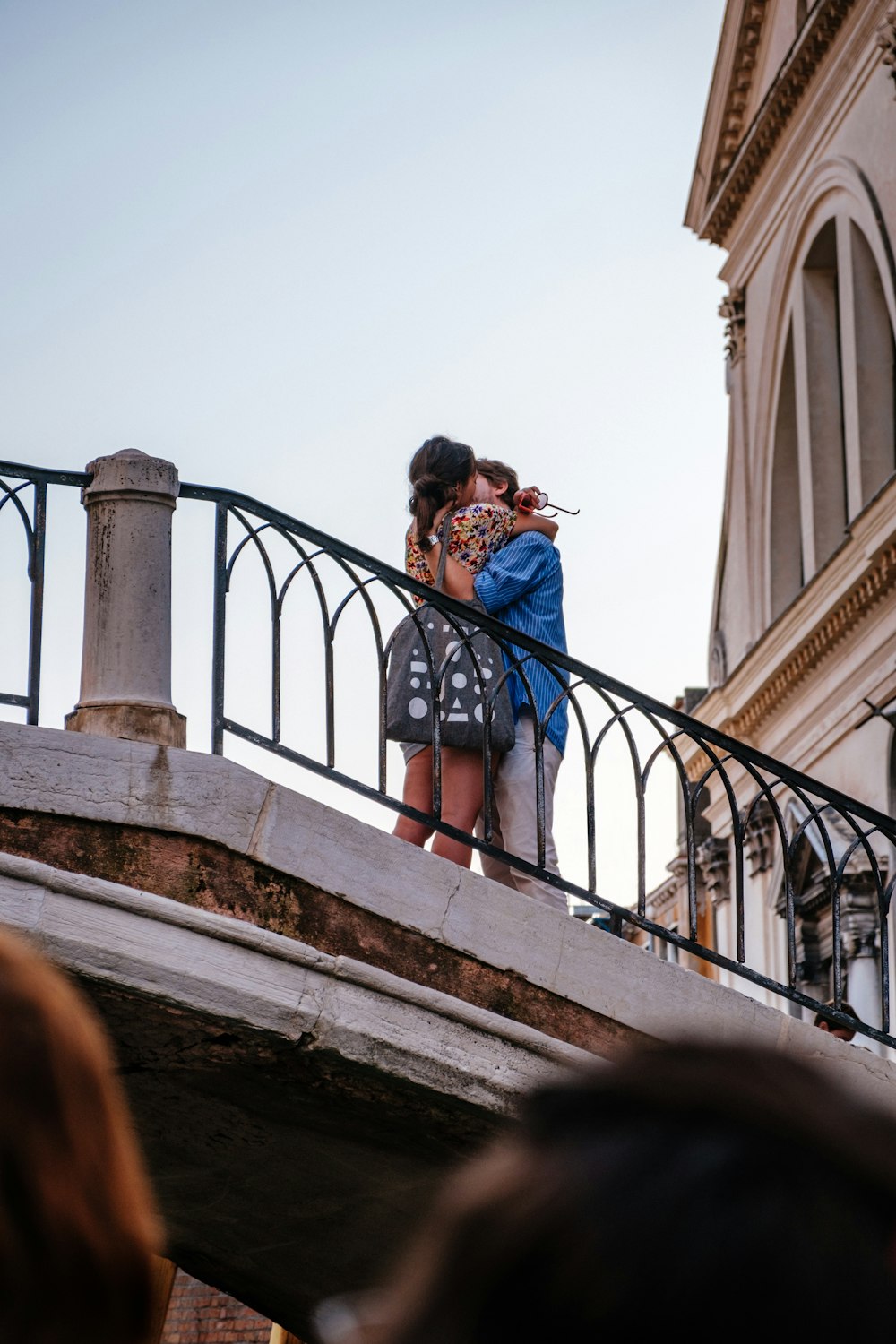 man and woman standing and facing each other while kissing on lips near black railings