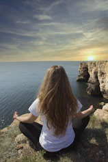 woman meditating on high mountain ground near sea during daytime