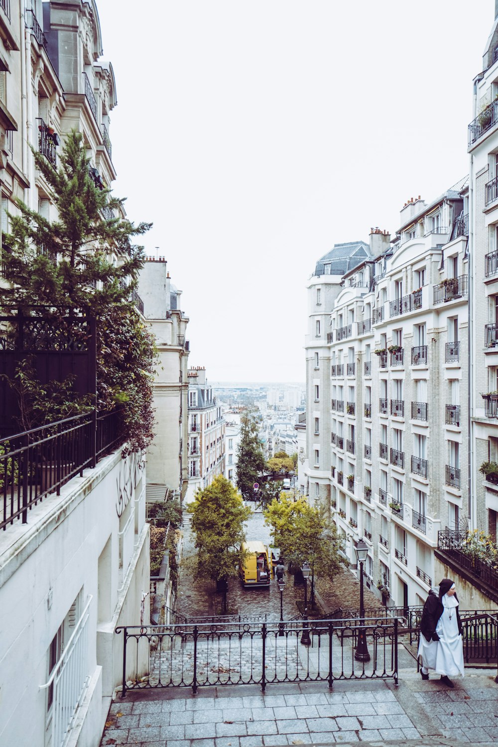 view photography of woman walking between white concrete building during daytime