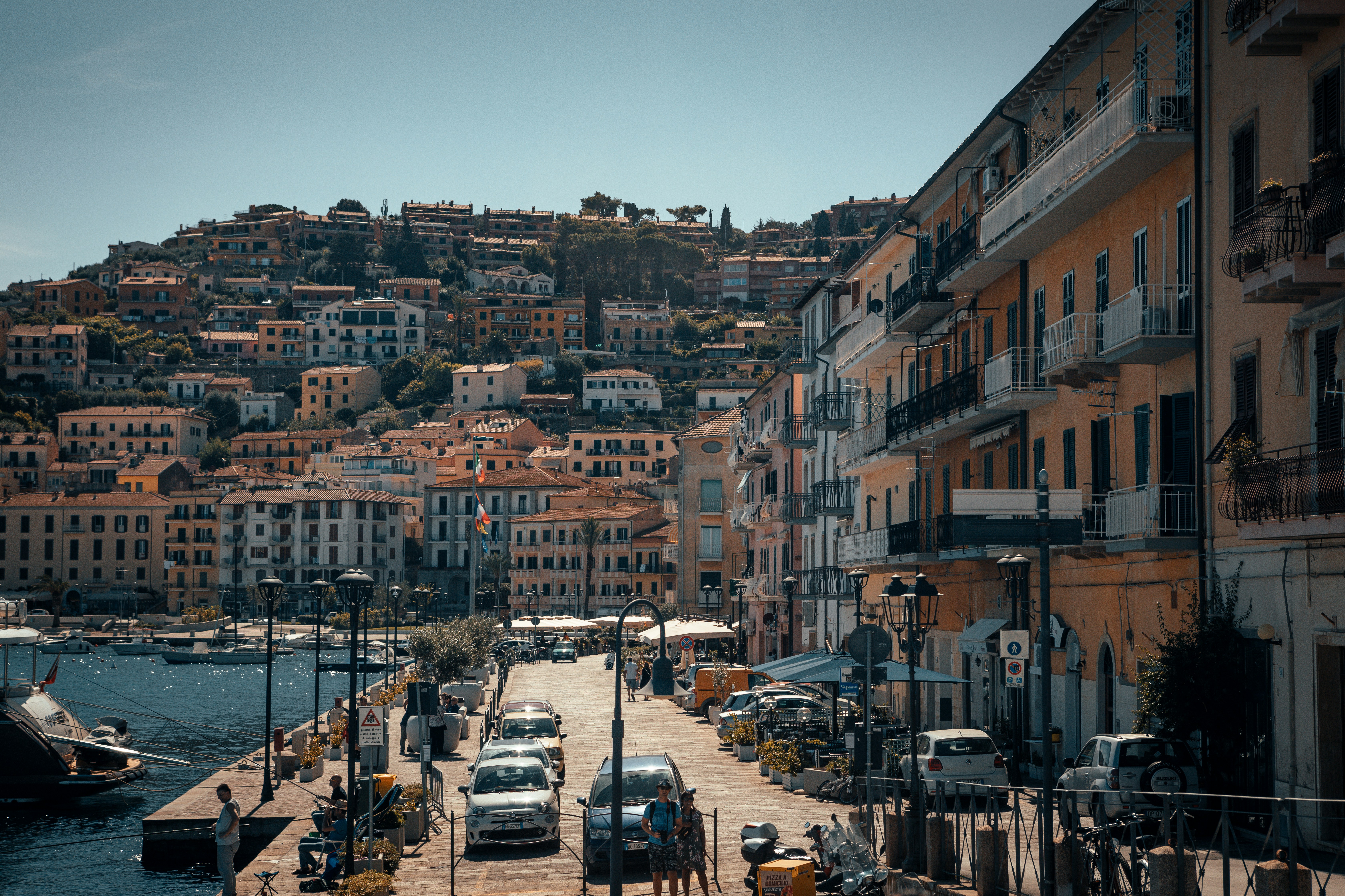 vehicles parking near building near body of water, A beautiful coastal town in Tuscany, Italy. 
