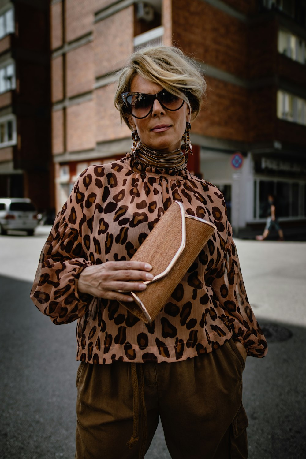 Femme portant un chemisier à manches longues léopard marron tenant une pochette marron debout
