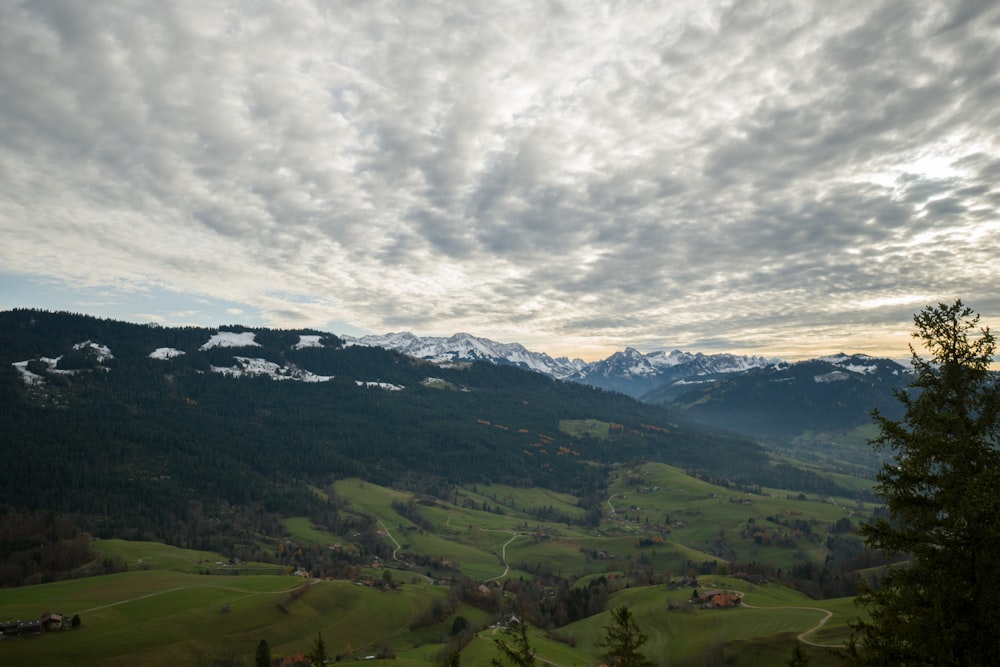 aerial photography of houses on green field viewing mountain under Cumulus clouds