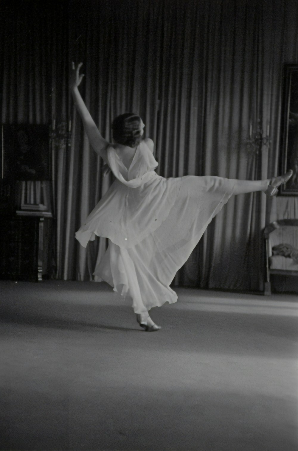 grayscale photo of woman dancing near curtains