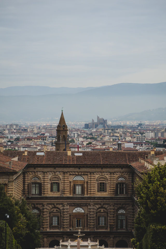 Palazzo Pitti's rusticated facade and bell tower seen from above with the Florence skyline and hills behind it.