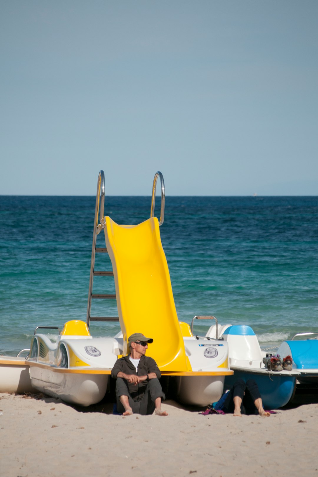 man sitting and leaning on white and yellow boat viewing blue body of water