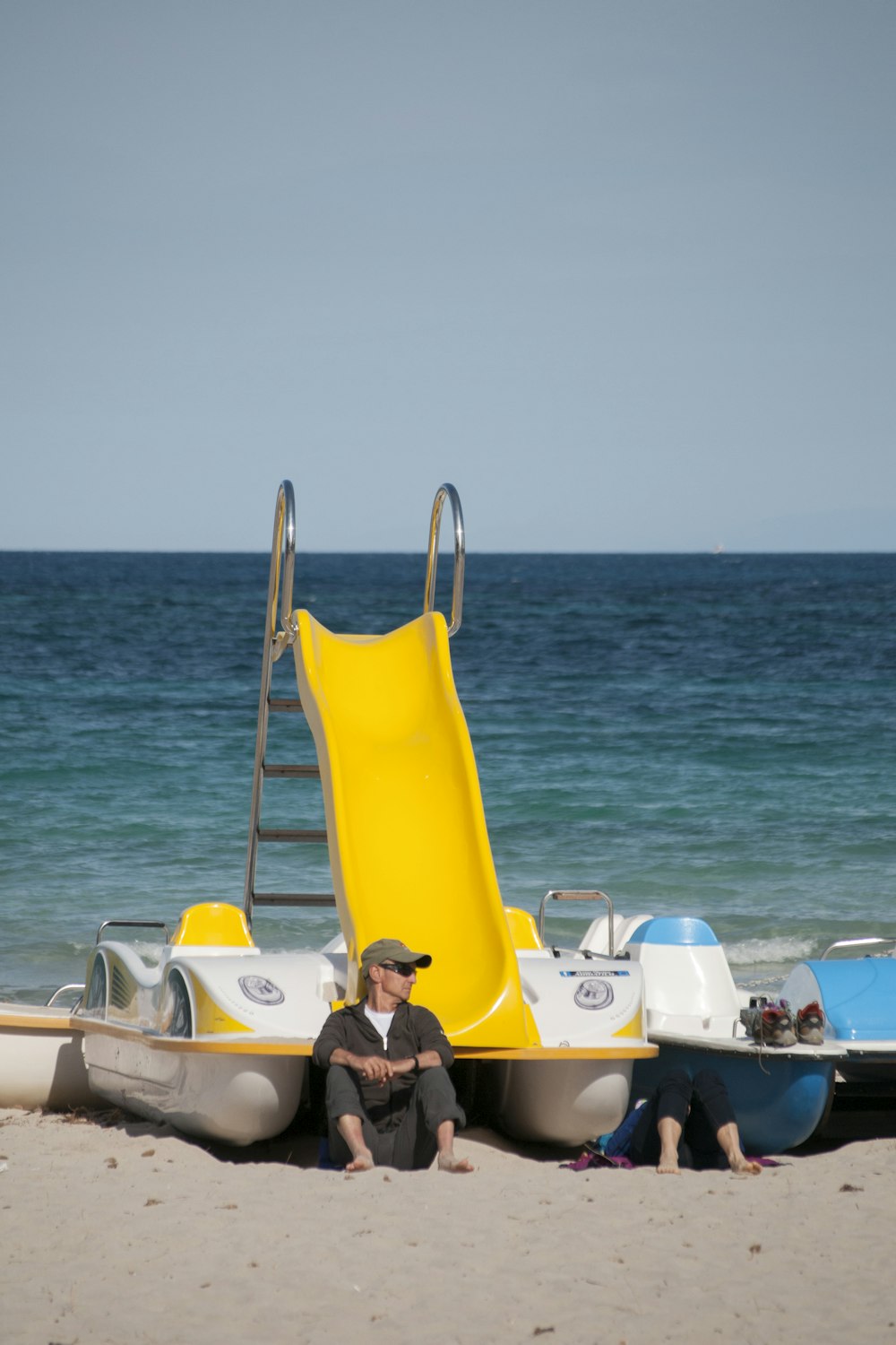 homem sentado e apoiado em barco branco e amarelo vendo corpo de água azul