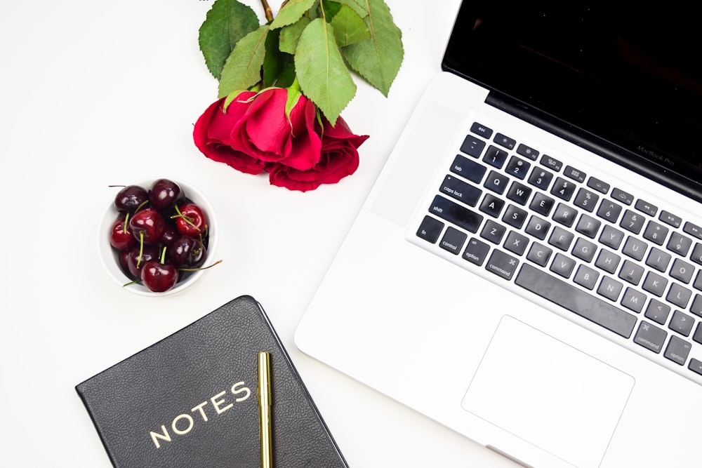 flatlay photo of rose, MacBook Pro, cherries, and black notebook