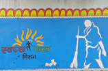 A mural features a stylized illustration of a person sweeping, along with vibrant sun motifs above the head and text in an Indian script. The artwork is predominantly blue and includes elements of orange, yellow, and green.