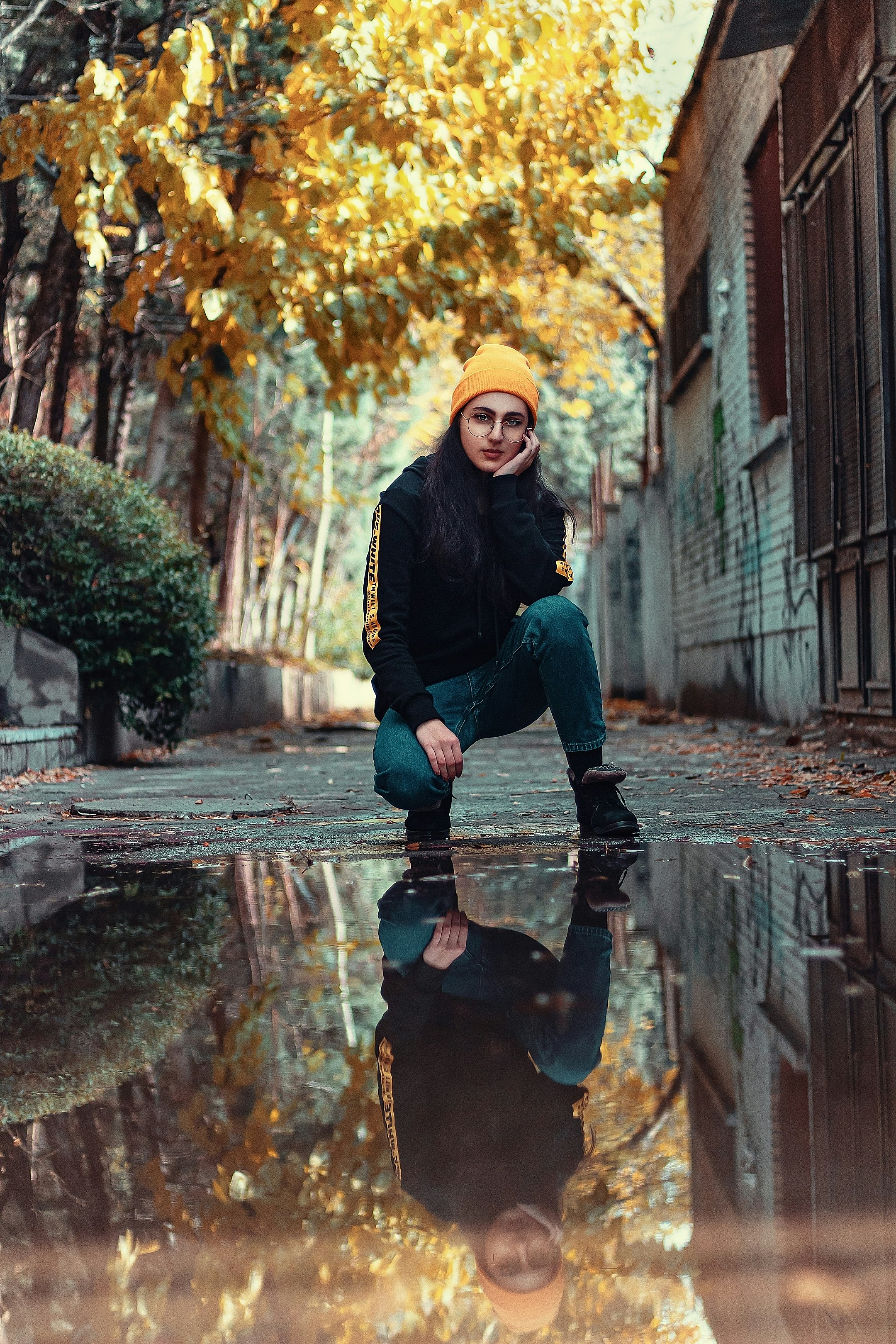 woman in black jacket, yellow beanie hat, and blue jeans kneeling on ground