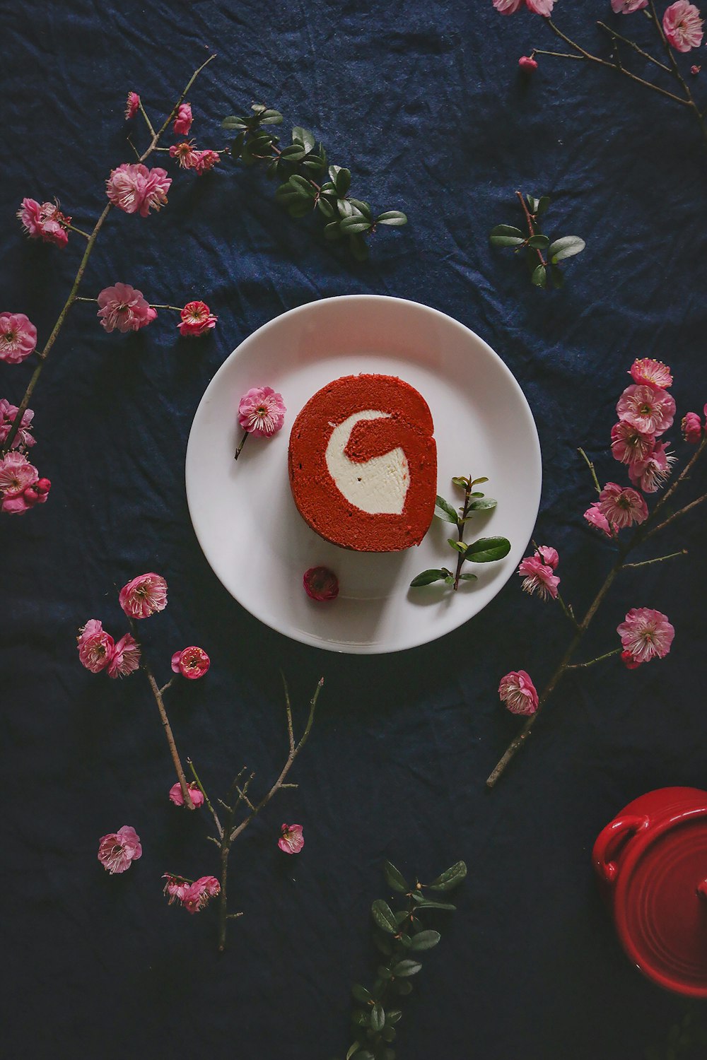 slice of cake on saucer on blue textile surrounded with flowers