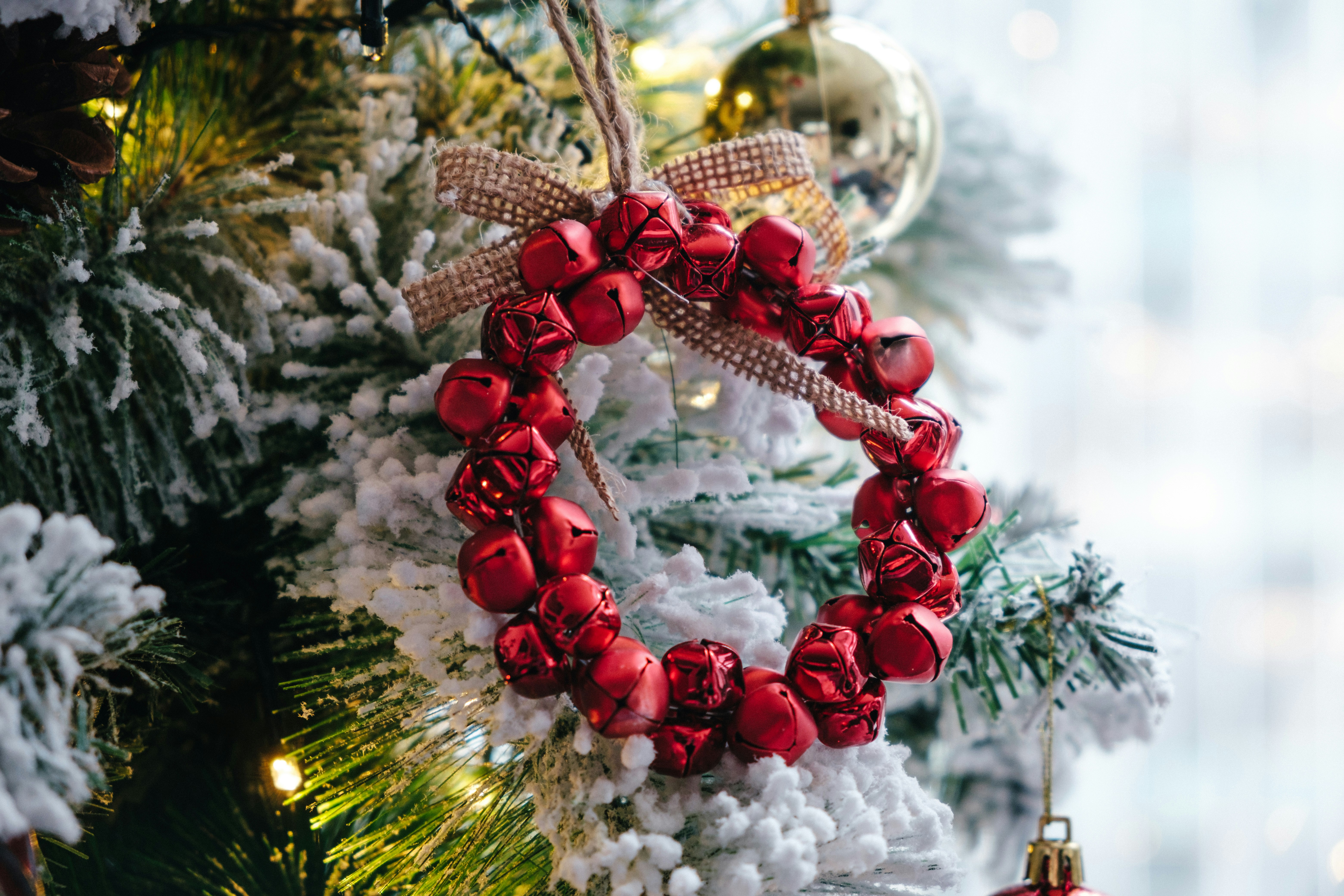 Close-up of a glossy red bead wreath on a snow-dusted Christmas tree, with warm bokeh lights in the background.