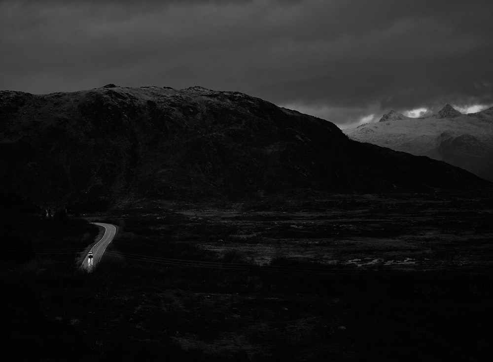 grayscale photography of cars on road by mountain under white skies