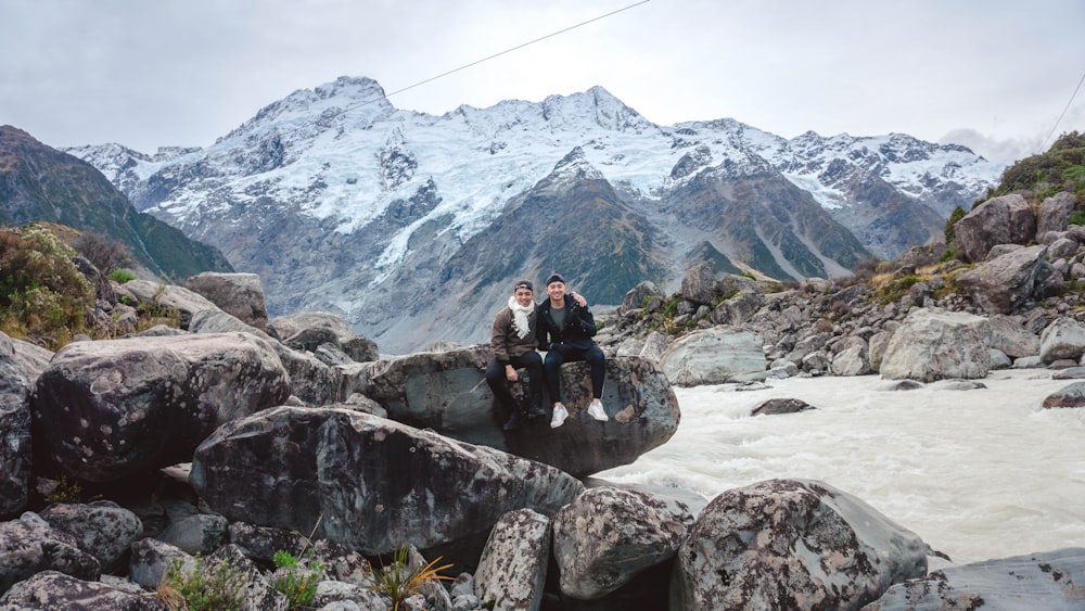 2 people sitting on rock by river at daytime