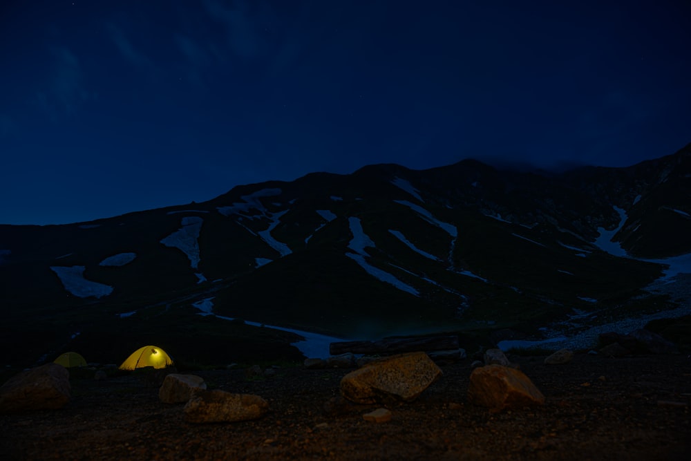 tents by rocks and mountains under white skies at nighttime
