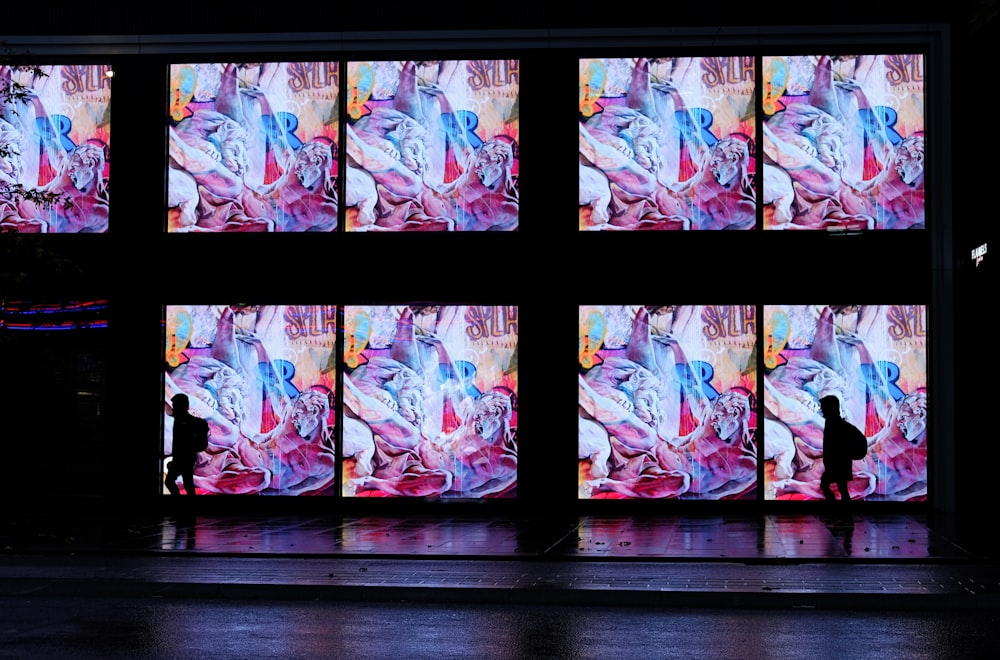 two persons walking beside building with LED artworks