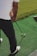 A person stands on a green artificial turf, holding a golf club, preparing to hit a yellow golf ball. The person is wearing a white shirt and dark pants with white and red shoes.