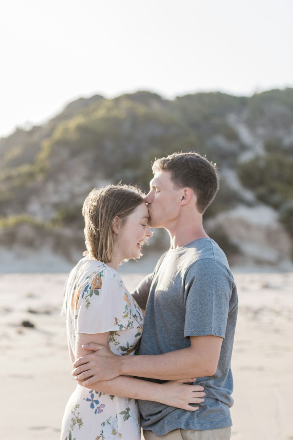 man kissing a woman on her forehead at shore during daytime