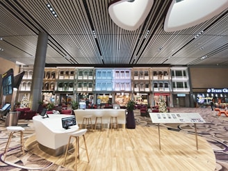 An indoor setting with a modern aesthetic, featuring a high, striped ceiling and walls that are designed to resemble traditional exterior building facades. The space includes contemporary seating arrangements, interactive screens, and digital kiosks. Christmas decorations, including a tree, are visible, suggesting a festive atmosphere.