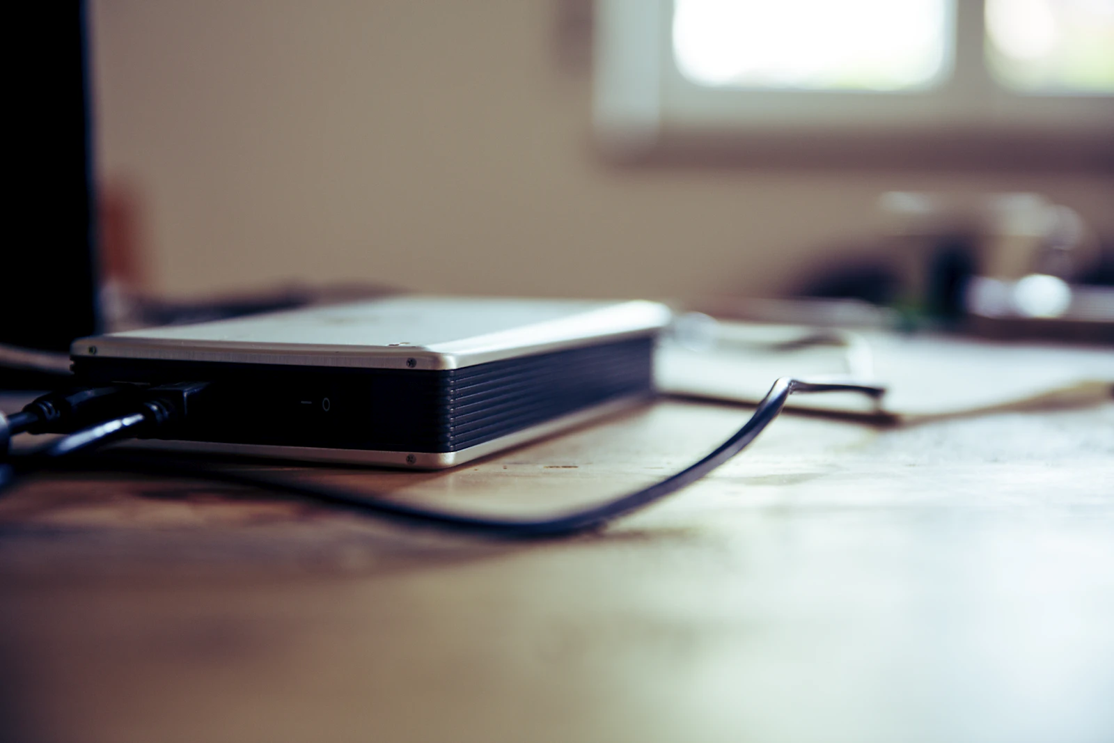 External hard drive with connected cables sitting on a wooden desk in soft window light