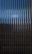 A series of vertical metal panels create a pattern with alternating light and shadow effects. The surface appears reflective with a play of light resulting in a dynamic visual texture.