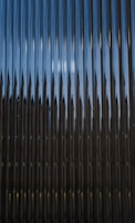 A series of vertical metal panels create a pattern with alternating light and shadow effects. The surface appears reflective with a play of light resulting in a dynamic visual texture.