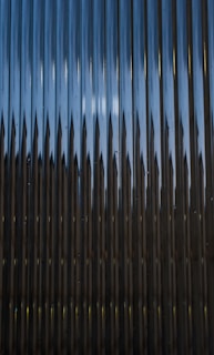 A series of vertical metal panels create a pattern with alternating light and shadow effects. The surface appears reflective with a play of light resulting in a dynamic visual texture.