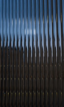 A series of vertical metal panels create a pattern with alternating light and shadow effects. The surface appears reflective with a play of light resulting in a dynamic visual texture.