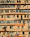 A multi-story residential building with numerous windows and balconies. Many air conditioning units are mounted on the walls, and clothes are hanging out to dry on some balconies. The building exterior is primarily orange and beige. A street lamp is visible, as well as street signs in the foreground.