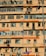 A multi-story residential building with numerous windows and balconies. Many air conditioning units are mounted on the walls, and clothes are hanging out to dry on some balconies. The building exterior is primarily orange and beige. A street lamp is visible, as well as street signs in the foreground.
