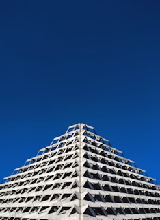 A triangular concrete building with a geometric pattern of protruding shapes against a clear, deep blue sky.