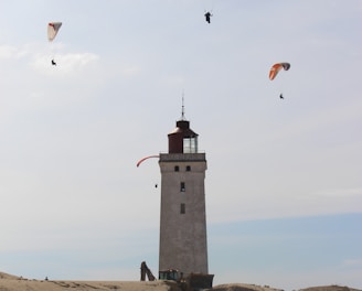 people paragliding above white and black lighthouse under white and blue sky