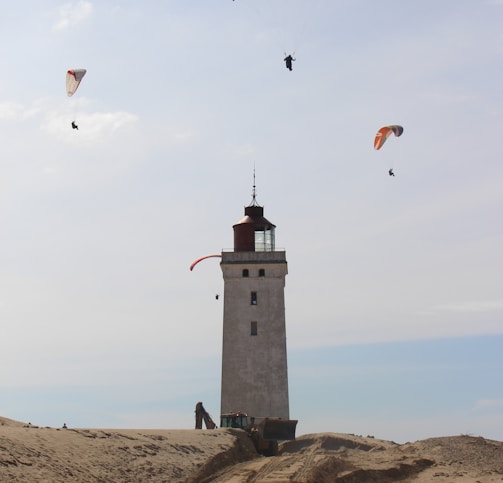 people paragliding above white and black lighthouse under white and blue sky