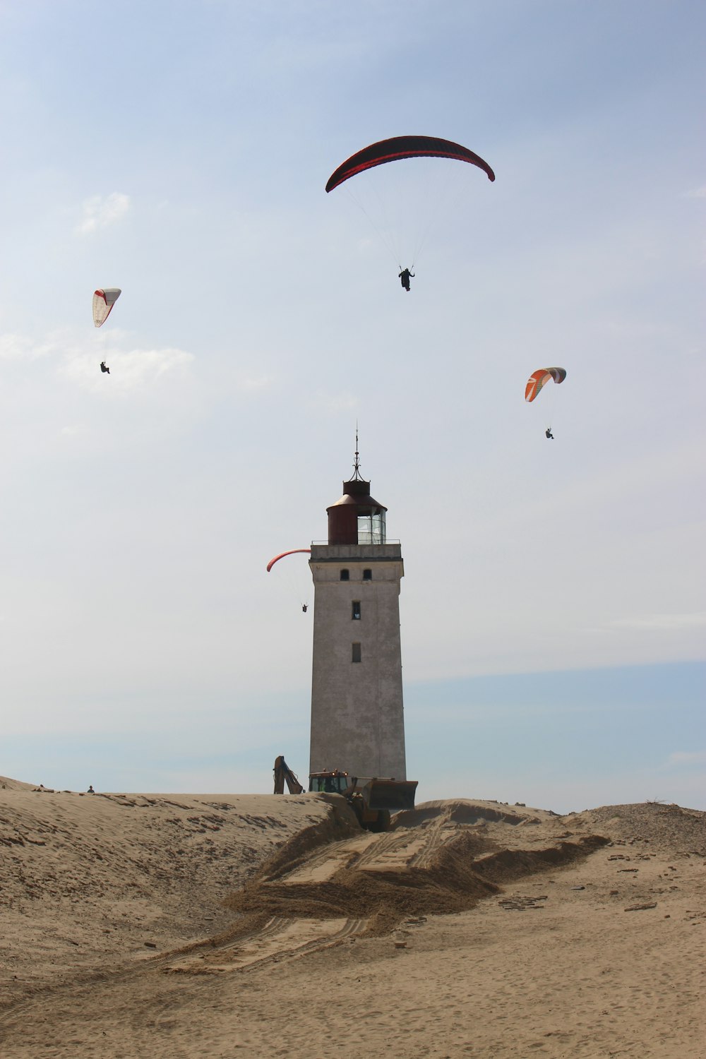 people paragliding above white and black lighthouse under white and blue sky