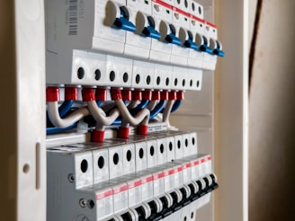 A detailed view of an electrical panel with multiple circuit breakers. The breakers are organized in rows with toggle switches and wiring connections. The wires are predominantly blue and white with red insulation at the terminals.