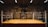 An empty boxing ring is set up in a dimly lit gym with various boxing posters adorning the walls. The ropes of the ring are slightly worn, and the space has an aged, rustic feel.