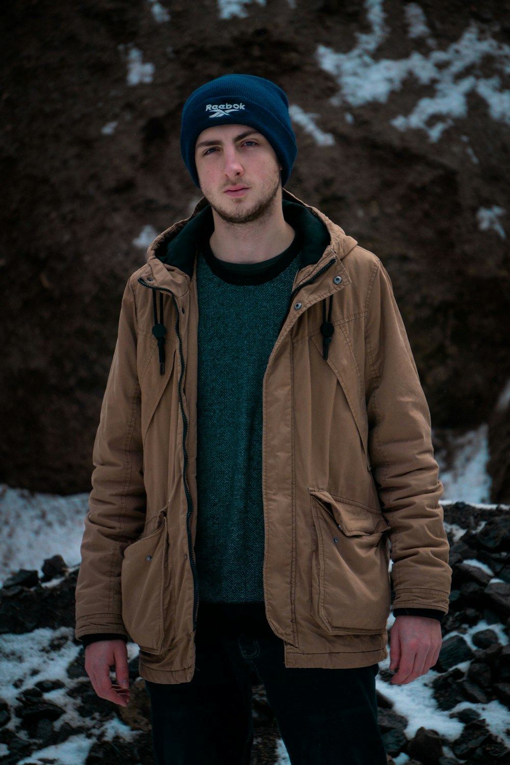 a man standing in the snow wearing a brown jacket