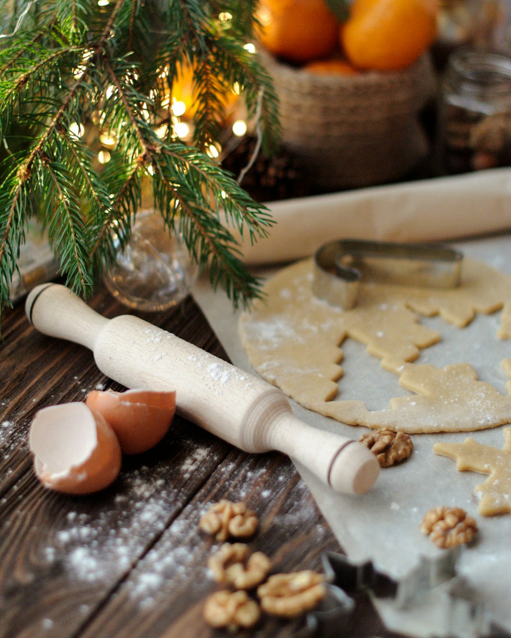 white wooden rolling pin near dough, egg shell, orange fruits, and walnuts