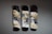Three skateboard decks are mounted on a wall, featuring abstract art with swirling patterns in black, white, and gold. The designs include bold, sweeping brushstrokes and intricate splatters that create a dynamic, fluid appearance.