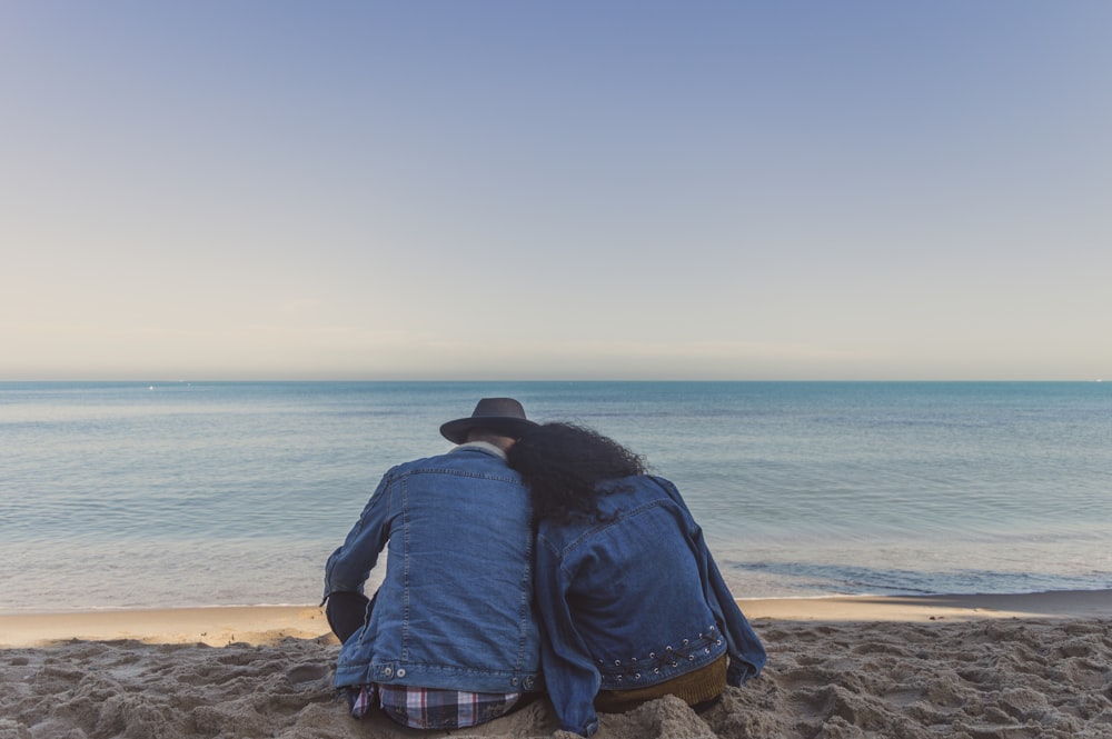 uomo e donna che si siedono sulla spiaggia di sabbia di fronte all'oceano durante il giorno