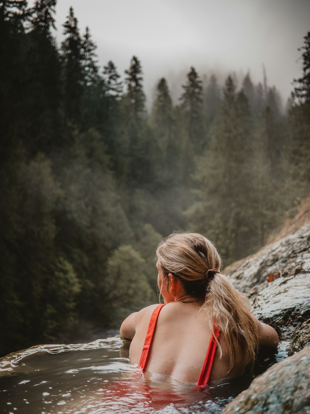 donna che indossa top bikini con spallina a spaghetti rossa sullo specchio d'acqua che osserva la montagna