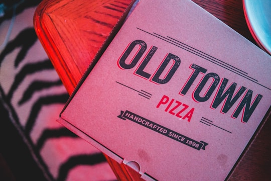 Close-up of a pizza box with floral patterns and promotional text blending two local businesses.
